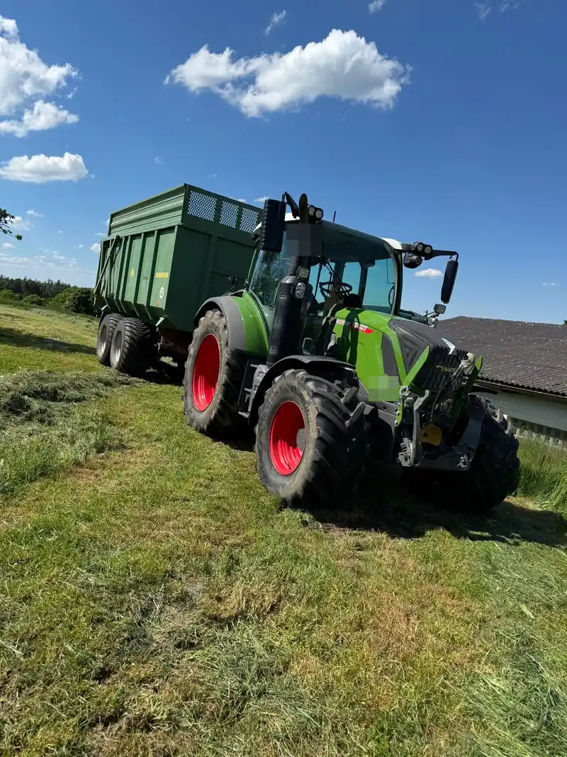 Schlepper mit Anhänger auf einer gemähten Wiese unter blauem Himmel