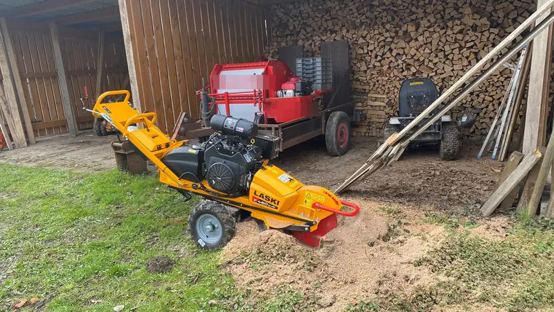 Wurzelfräse beim Fräsen vor einem Holzschuppen