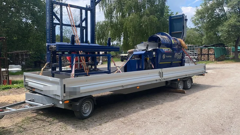 Sägespalter auf dem Anhänger am Holzplatz, dahinter Gitterboxen mit Brennholz