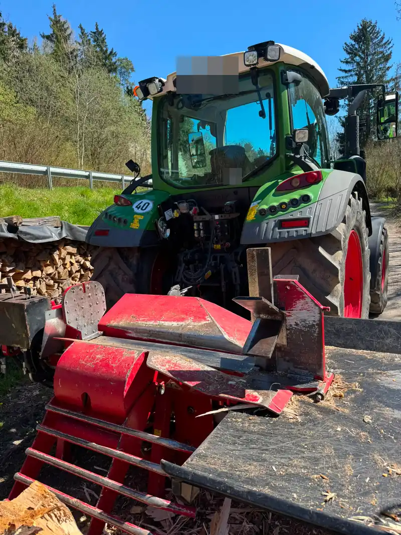 Holzspalter am Schlepper vor aufgeschichtetem Brennholz
